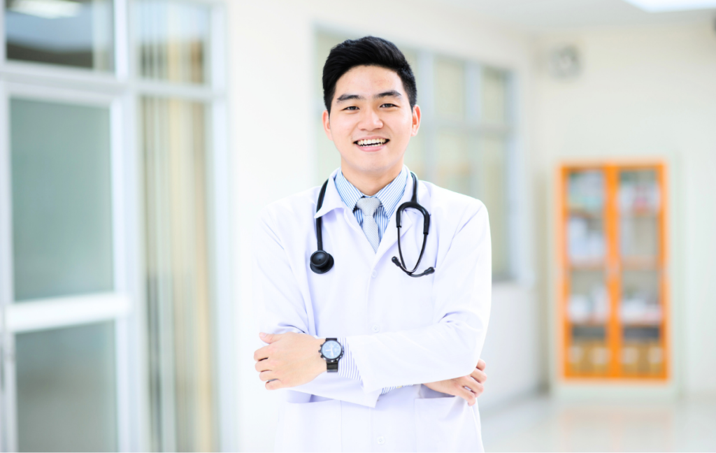 A smiling, professional male surgeon in a white medical coat, representing the high standards of finding the right cosmetic surgeons in Vietnam.