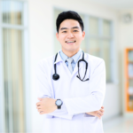 A smiling, professional male surgeon in a white medical coat, representing the high standards of finding the right cosmetic surgeons in Vietnam.