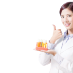 A smiling female dentist in a lab coat holding a dental implant model and giving a thumbs up, representing high-quality Full mouth dental implants in Vietnam.