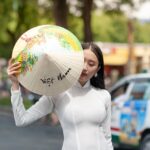 A woman in a white Ao Dai holding a traditional Vietnamese conical hat (Non La) offering medical concierge in Asia