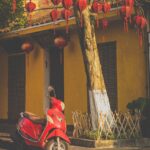 A classic red motorbike parked in front of traditional red lanterns, capturing the cultural charm of Vietnam for luxury medical travelers getting surgery abroad solo.