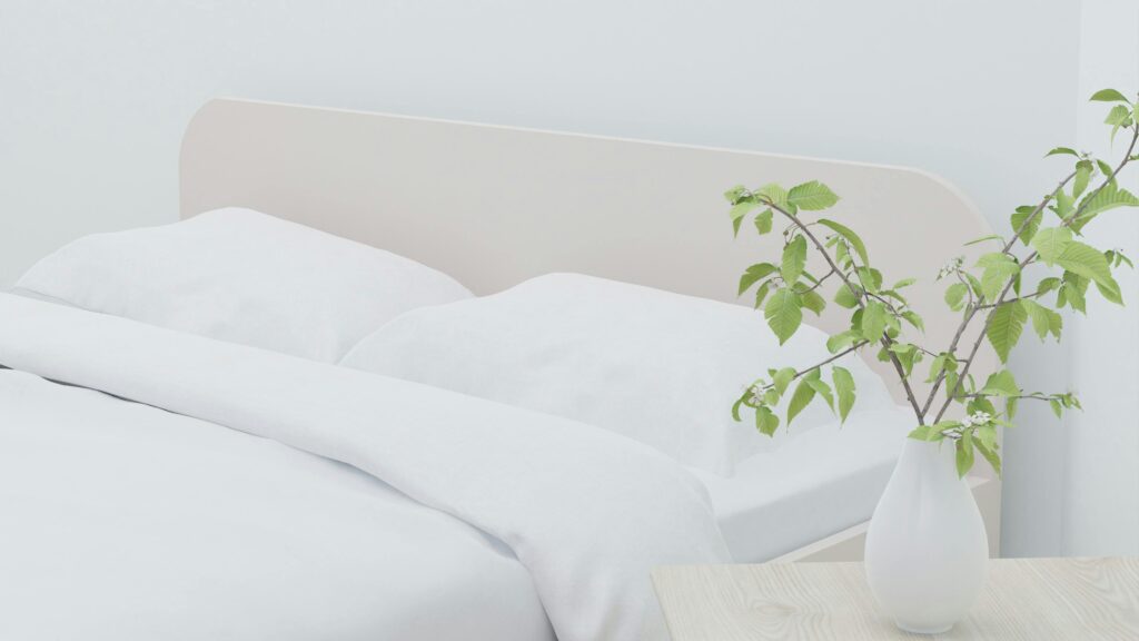 Light and airy modern bedroom with white bedding and a vase of greenery on a wooden table.