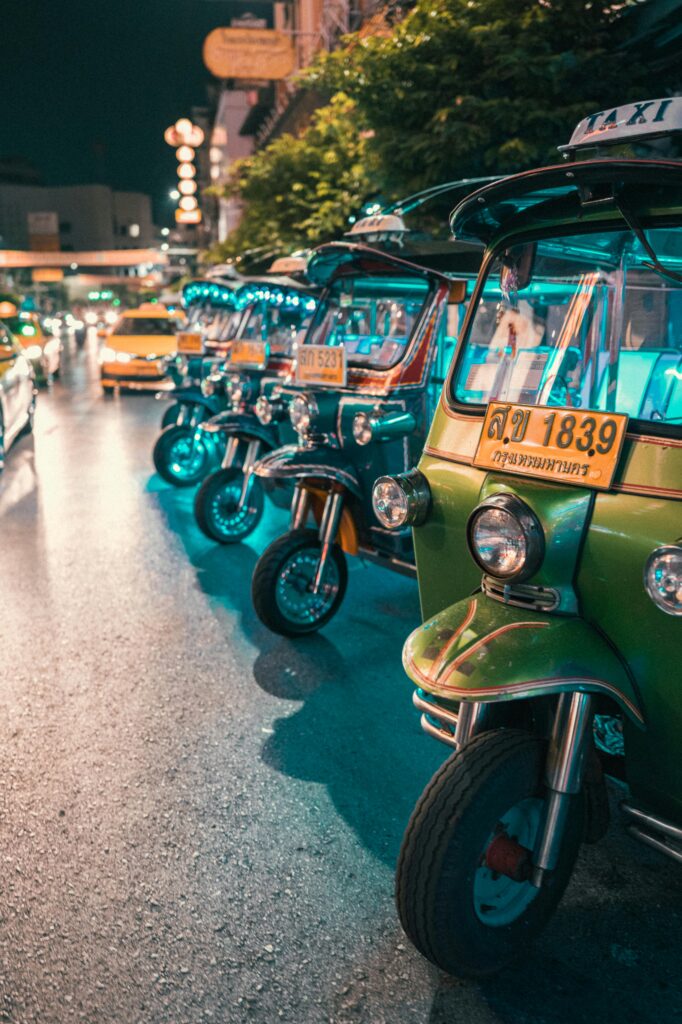 Colorful tuk tuks lined up on a bustling Bangkok street at night with vibrant lights. Vietnam vs Thailand for Cosmetic Surgery