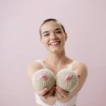 Cheerful young woman with short hair holding knitted breasts, promoting gender-affirming surgery in Vietnam.