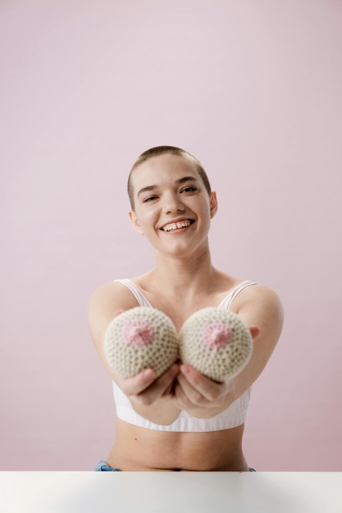 Cheerful young woman with short hair holding knitted breasts, promoting breast cancer awareness.
