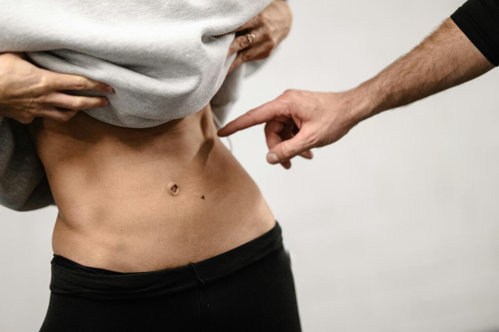 Body Contouring with Fat Grafting in Vietnam 2 An intimate close-up of a person's toned abdominal area with a hand pointing, emphasizing fitness.